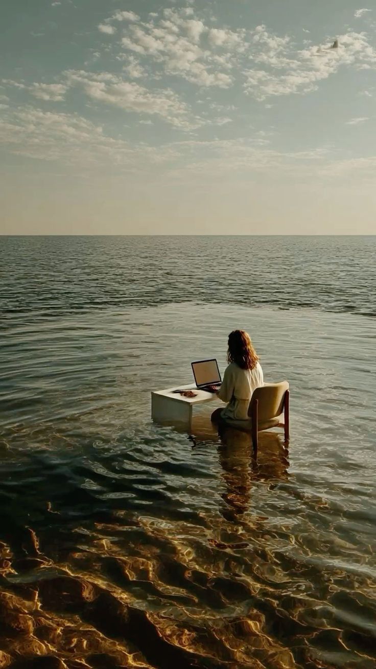 A person working at a desk and chair set up in the shallows of the sea